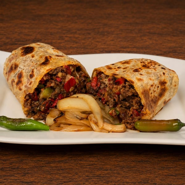 Two halves of a grilled burrito filled with meat and vegetables, served with onions and peppers.