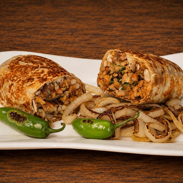 Two burritos, cut in half, revealing a savory filling, served with grilled onions and green peppers.