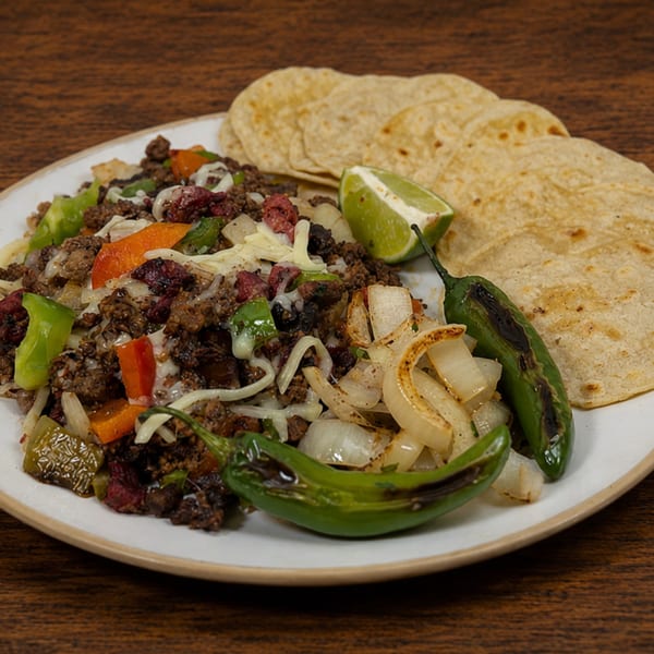 A plate of carne asada with grilled onions, peppers, lime, and tortillas on a wooden table.